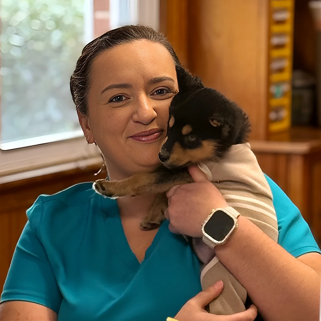 Whitney Schmidt – Woman in teal scrubs holding a small black and tan puppy wrapped in a towel.